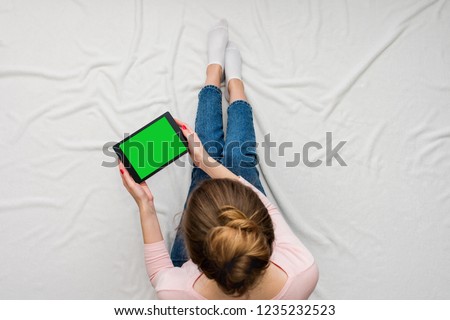 Woman holding a tablet, women's feet, sitting on a white crumpled blanket. Women's hands. Background with copy space, for advertisement. Top view