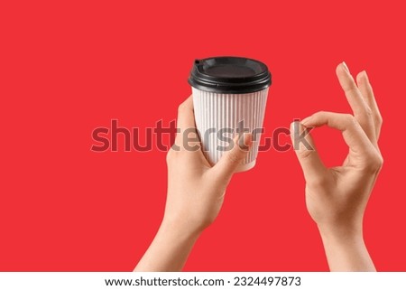 Woman holding takeaway cup of coffee and showing OK gesture on red background