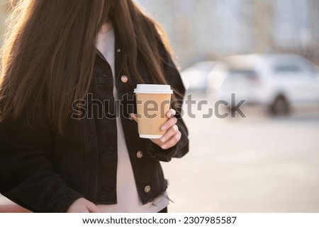 woman is holding a takeaway cup of hot drink outdoors on a summer day in the city