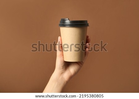 Woman holding takeaway paper coffee cup on brown background, closeup