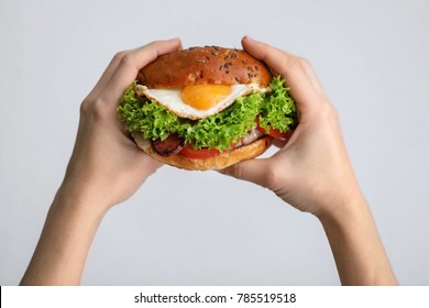Woman holding tasty burger with fried egg on light background