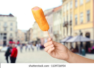 Woman Holding Tasty Corn Dog On City Street