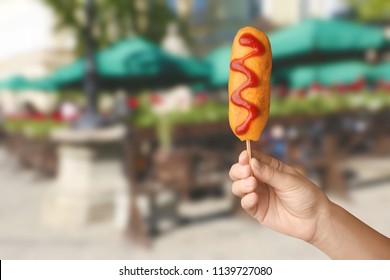 Woman Holding Tasty Corn Dog With Ketchup On City Street