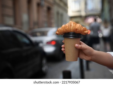 Woman holding tasty croissant and cup of coffee on city street, closeup. Space for text - Powered by Shutterstock