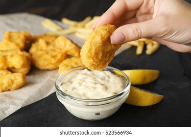 Woman holding tasty nugget and bowl with sauce on table, closeup