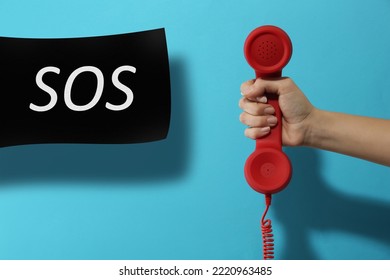 Woman Holding Telephone Handset On Light Blue Background, Closeup. Emergency SOS Call