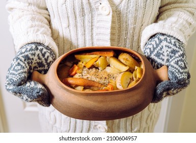 Woman Holding Terracotta Clay Cooking Pot With Slow Cooked Pork Roast And Vegetables Inside. Wearing Knitted Clothing, Winter Comfort Food Concept.