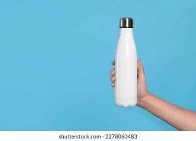 Woman holding thermo bottle on light blue background, closeup. Space for text