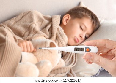 Woman Holding Thermometer With High Temperature And Sick Child Lying On Couch At Home