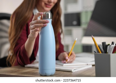 Mujer sosteniendo una botella de termo en el lugar de trabajo, cerrando