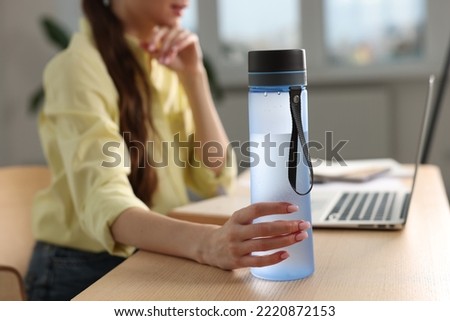 Woman holding transparent bottle at workplace indoors, closeup