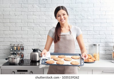 Woman holding tray with cookies in kitchen. Fresh from oven - Powered by Shutterstock