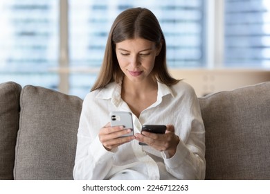 Woman holding two modern smart phones seated on couch, owner of new wireless gadget transfers data, contacts, files and photos from old model of device, compares software, use technology and back up - Powered by Shutterstock