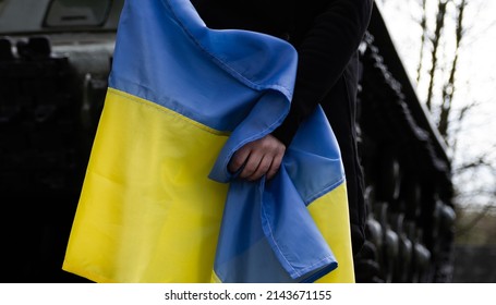 Woman Holding Ukrainian Flag, With Battle Tank In Background. Russia Invasion, War In Ukraine, Crisis Concept. Girl Standing In Front Of Military Armored Fighting Vehicle.