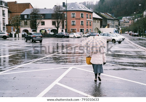 Woman holding an umbrella on a wet and empty\
parking lot in the town of La Roche-en-Ardenne in the Ardennes\
region of Belgium