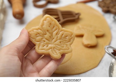 Woman holding unbaked leaf shaped cookie at white table, closeup - Powered by Shutterstock