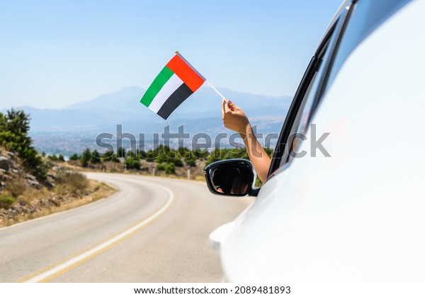 Woman\
holding United Arab Emirates flag from the open car window driving\
along the serpentine road in the mountains.\
Concept