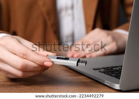 Woman holding usb flash drive near laptop at wooden table, closeup