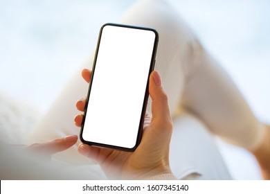 Mujer sosteniendo y usando un smartphone en casa. Tragamonedas para teléfono móvil con pantalla blanca vacía.