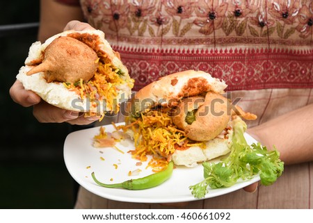 Woman holding Vada Pav/paav in her hand usually served with sweet/green chutney.  Indian fast/street food snack, North India, Maharashtra. vada sandwiched between two slices/lloaf of bread.
