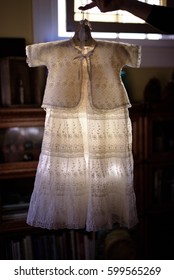 Woman Holding Up Vintage Lace Family Baptism Dress In Early Morning Sunlight