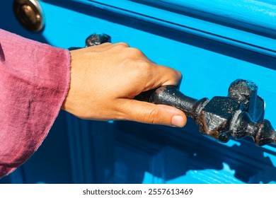 Woman holding a vintage metal door handle of a blue door. Opening the door. - Powered by Shutterstock