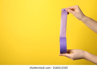Woman holding violet adhesive tape on yellow background, closeup. Space for text - Shutterstock ID 2160111545