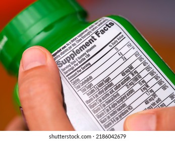 A Woman Holding A Vitamin Supplement Jar With A Supplement Facts Label At The Back.