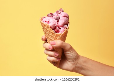 Woman holding waffle cone with delicious raspberry ice cream on color background