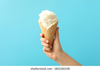 Woman holding waffle cone with delicious ice cream on light blue background, closeup