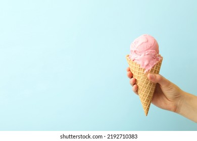 Woman holding waffle cone with delicious pink ice cream on light blue background, closeup. Space for text