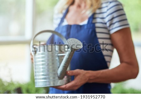 Woman holding watering can in hands standing in greenhouse