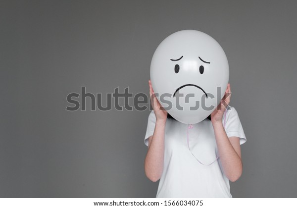 A woman holding white balloon with sad smile face\
emotion instead of head. Negative Thinking concepts. Girl holds a\
balloon in her hand
