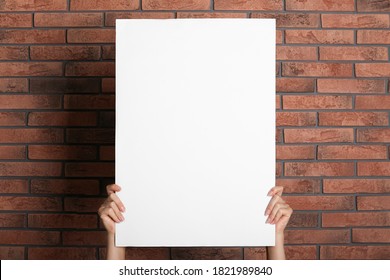 Woman Holding White Blank Poster Near Red Brick Wall, Closeup. Mockup For Design