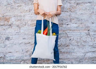 Woman Holding White Canvas Tote Bag With Vegetables Near Brick Wall.