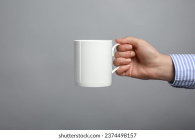 Woman holding white mug on light grey background, closeup. Space for text