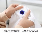 Woman holding white shirt with blue ink stain on blurred background, closeup