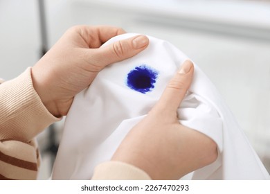 Woman holding white shirt with blue ink stain on blurred background, closeup