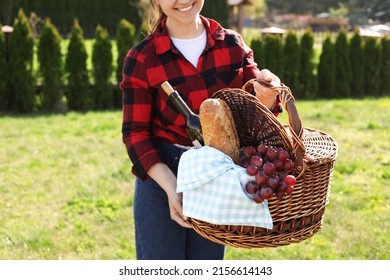 Woman Holding Wicker Basket With Wine And Snacks In Park, Closeup. Picnic Season