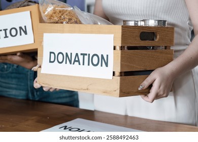 Woman holding a wooden donation box filled with food items, promoting community support and charitable efforts.