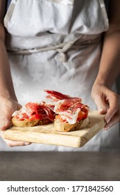 Woman holding wooden try with toasted bread slice with fresh tomatoes and cured ham. Delicious appetiser Italian prosciutto and Spanish Iberian ham snack