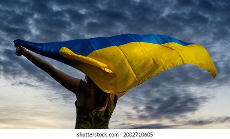 Woman Holding A Yellow And Blue Flag Of Ukraine On A Background Of Dark Cloudy Sky.