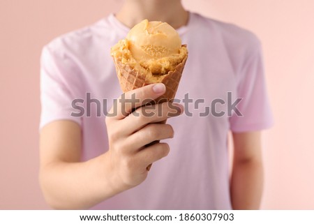 Woman holding yellow ice cream in wafer cone on pink background, closeup