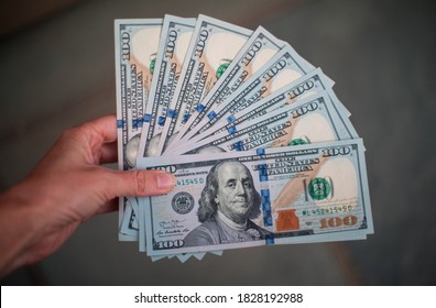 A woman holds 1,000 US Dollars in the form of ten 100 Dollar bills.