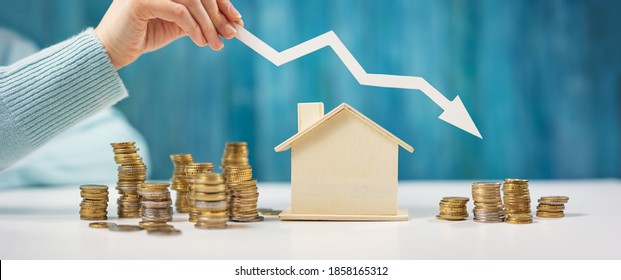 Woman Holds An Arrow Down Over Model Of The House And Stack Of Coins. Concept Of The Crisis In The Real Estate Market.