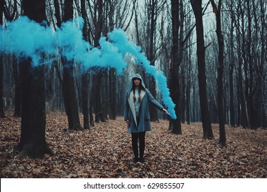 Woman Holds Up Blue Smoke Flare To Signal For Help In The Middle Of Nature. Rainy Forest In Mist. 