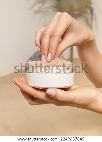 Woman holds body scrub in plastic jar. Sugar scrub for body, face. Summer skin care