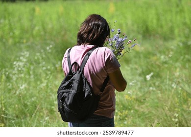 Woman holds a bouquet of wild flowers. bouquet in a woman's hand glow in the sun. girl in nature. walk in summer, sunny day. spring season. back view. close-up - Powered by Shutterstock