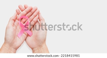 Woman holds bow made of pink ribbon - symbol of breast cancer awareness. World Cancer Day concept on white background with copy space.