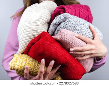 A woman holds bright warm winter sweaters. Closet cleaning. Donations. Close-up. Selective focus.